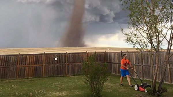 Man mowing a yard with a tornado in the background. 
