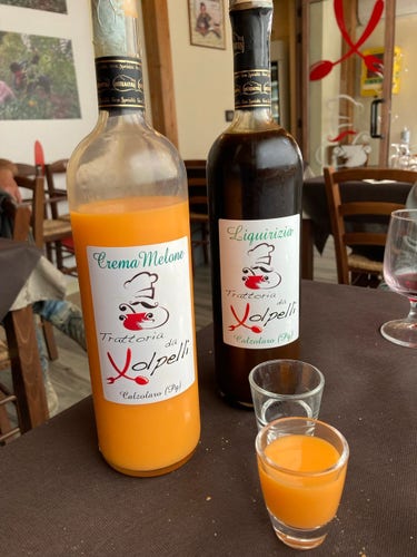 Two bottles on a restaurant table with two shot glasses. One has an orange colored liqueur and the other is brown. The labels bear the restaurant logo for Trattoria da Volpelli. 