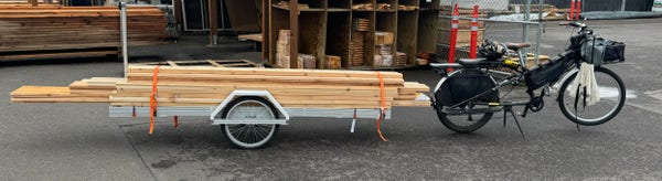 My cargo ebike, with a trailer attached that has a number of 8, 10, and 12 foot long boards of lumber loaded on it.