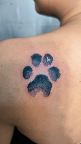 Tattoo of a dog's paw in a dot shading style with a heart cutout on one of the digits