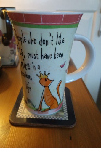 Large mug of tea on a bedside cabinet 
With a ginger cat at the bottom left wearing a yellow crown over one earlier 