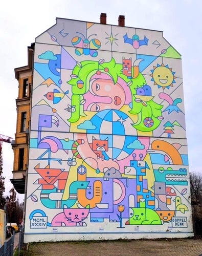 Streetartwall. A mural with a friendly Mother Earth and many different figures in pop art style was sprayed/painted on the outside wall of a four-storey building. In the center is a female figure with neon green hair embracing a kind of globe in a blue and white diamond pattern. She is surrounded by countless animals. A veritable Noah's Ark covers the wall. There are cats, snakes, birds, fish and the sun, stars and much more. The mural is marked with the Roman numeral MCML XXXIV (1984). A wonderful hidden object picture, designed with naïve cheerfulness, in front of which you can spend a lot of time taking it all in.