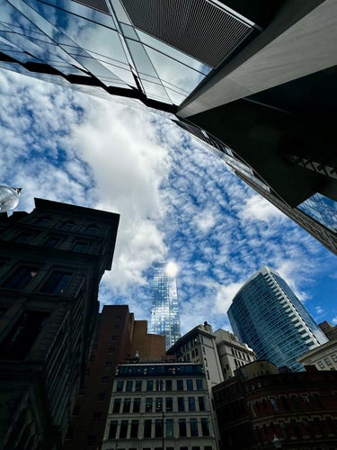 A wide angle view looking up towards a glass walled building with the sun reflecting off it, the rest of the building lost against the sky, distorted looking building fill the top and bottom of the shot