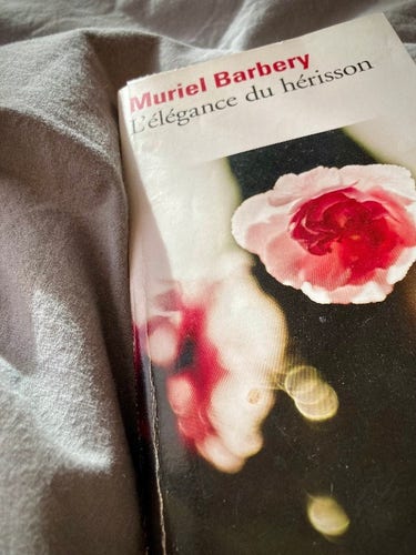 Sur un duvet gris, le livre L'élegance du hérisson, de Muriel Barbery. Il y a des fleurs roses en couverture. #VendrediLecture ©GD24