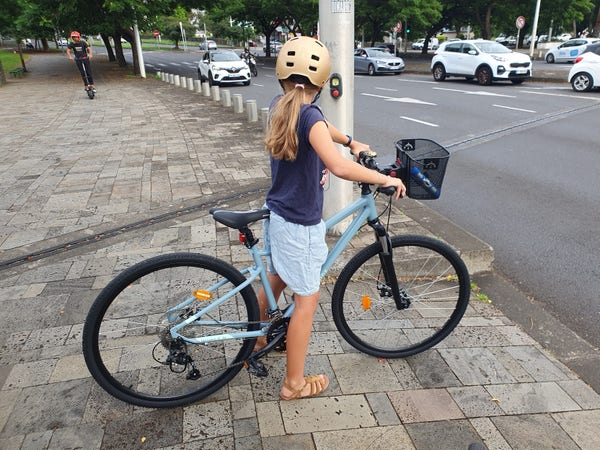 Une jeune fille avec un casque doré attend au feu sur un vélo bleu gris