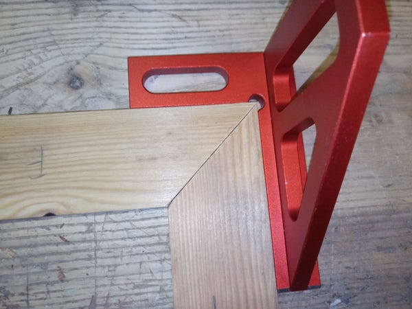 A piece of wood, cut in two pieces at a 45° angle. One piece is flipped over and held against the other half of the cut, forming a 90° angle if the saw is calibrated well. A red square is held against the two pieces and they're nicely fitting, at last.