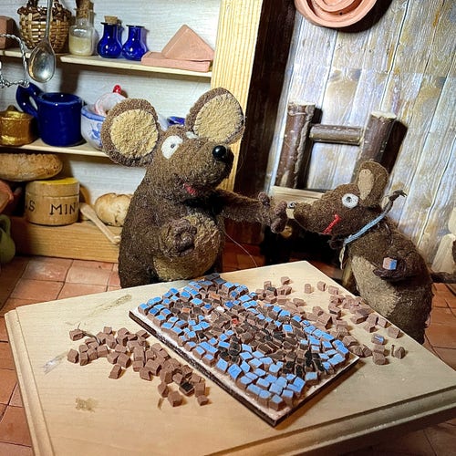 Photo of Minimus and Silvius, the Latin mice, mending a mosaic made of mouse-sized tiles. Silvius is holding a blue tile in his paw. The mosaic is a portrait of a mouse (of course)