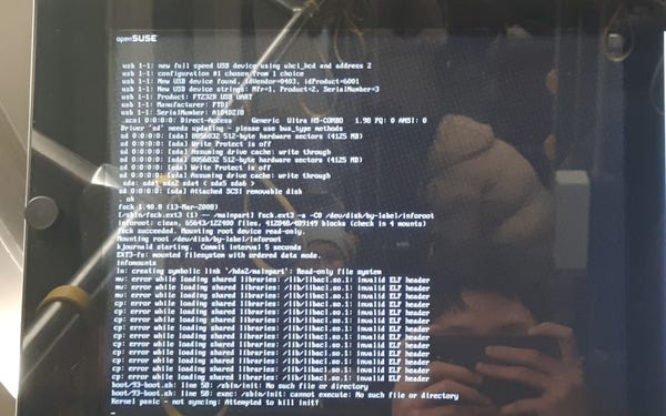 Picture of a display on the inside of a tram that usually displays the next stops. The system on the display seems to have crashed, and it now shows an OpenSUSE logo and a Linux crash log.