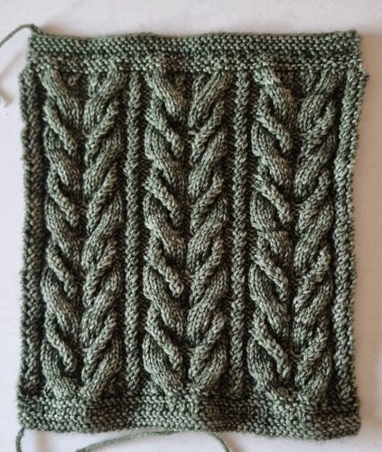 30cm knitted square with a pattern of twisted lines & 3 sets of R & L facing cables. Colour of hand dyed yarn is light olive green.