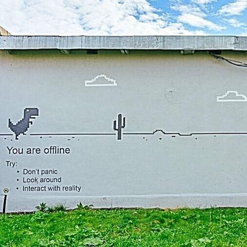 Wall art of a dinosaur in a pixel game scene of desert and tiny clouds, with the slogan You are Offline, Dont panic, Look around, Interact with reality

