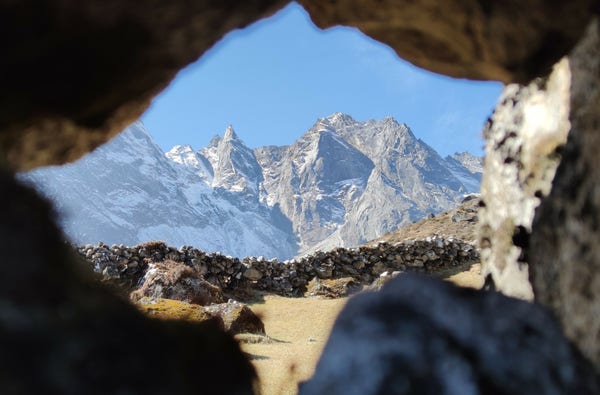 A collection of snowy peaks viewed through a hole in a stone fence.