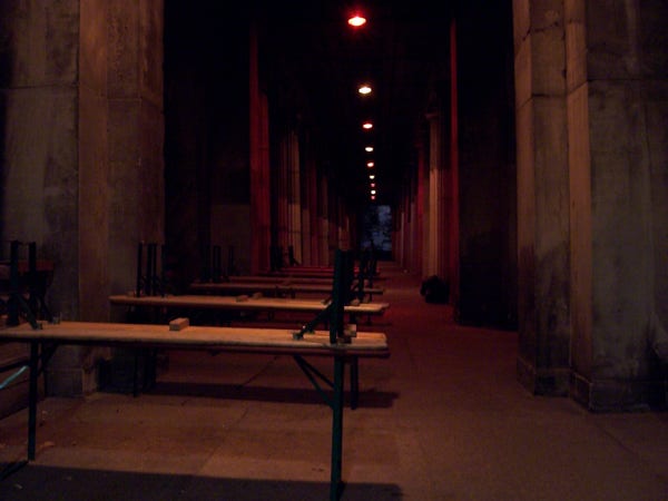 Night photo

view through a colonnade 

at the left beer banks, feet up, on long tables