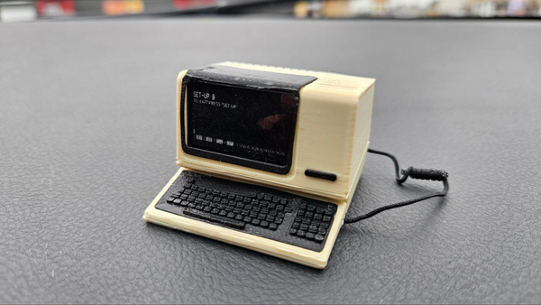 A tiny 3d printed DEC VT100 terminal. It is sitting at the setup screen on the dashboard of a car.

The tiny keyboard is attached to the tiny terminal with a tiny cable.

trust me it's adorable