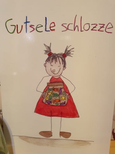 Postkarte mit einer Zeichnung von einem Mädchen, das ein Bonbonglas in den Händen hält und sich die Lippen leckt. Darüber steht "Gutsele schlozze". Alles ist im Stil einer Kinderzeichnung.
