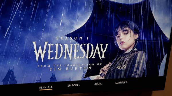 Photo of my tv showing the disc menu for Wednesday season 1. It has the image of Jenna Ortega as Wednesday holding an umbrella in the pouring rain, i.e. the funeral scene.