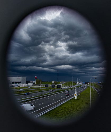 A portrait format picture taken through a hole in the metal windbreak screen on the  Philippus Oythovenpad bridge over the A4 motorway in Leidschendam. The picture shows a heavy storm coming from the south, over the Forepark industrial estate.