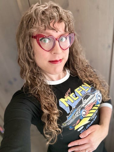 Me in a black back to the future dress with read heart-shaped glasses, long brown curly hair, and curly bangs