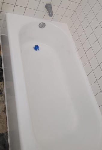 Clean looking tub with white caulking around it. Blue tape on the drain plug still visible.
