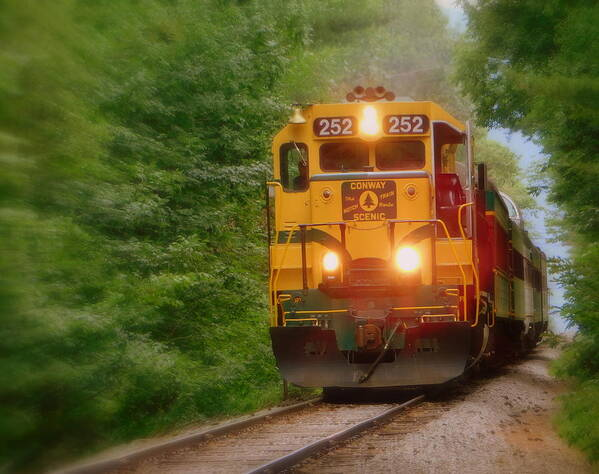 A photograph of the locomotive of the Notch train of the Conway Scenic Railroad.  The locomotive is gold in color.  There are two brightly shining headlights beaming as the train nears