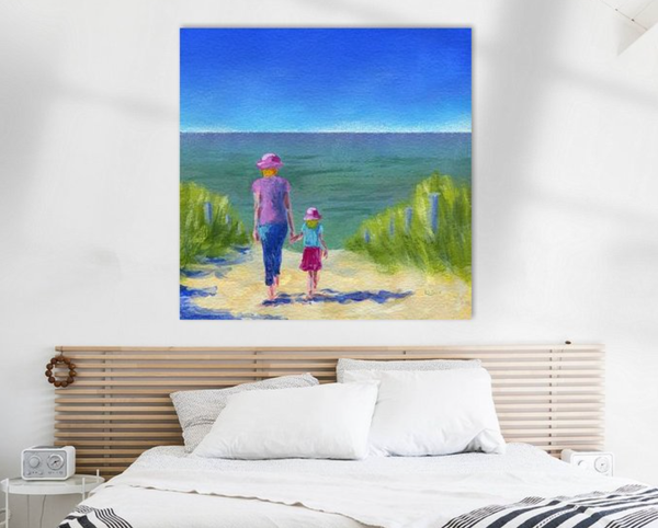 Together walking through the sand dunes is an acrylic painting in a contemporary square format by artist Karen Kaspar. A woman walks hand in hand with a little girl through sandy dunes to the beach. You can see the woman and the girl from behind. The woman is wearing blue pants and a purple t-shirt. The girl wears a light blue t-shirt and a pink skirt. Both wear pink hats with blond hair peeking out. The path to the beach is lined left and right by green seaweed. In the background, the sea stretches out in shades of blue and teal under a blue summer sky.
The painting hangs in a bedroom above a bed.
