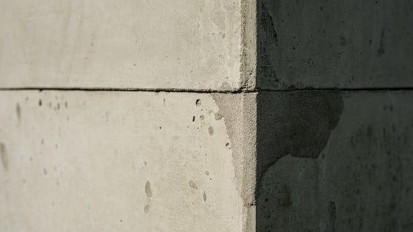 Close view of a vertical corner of two concrete blocks one on top of the other. The top corner of the lower block has been visibly repaired. The left hand faces are in sunlight, the right in shadow