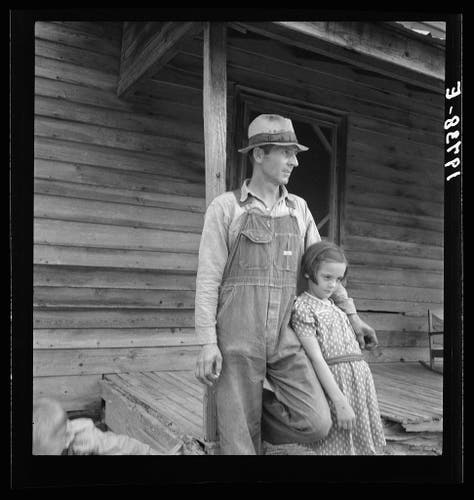  The image is a vintage photograph, possibly from the 1930s or 1940s, depicting a sharecropper with his oldest daughter. They are standing outside a wooden cabin that appears to be in Person County, North Carolina. The man is dressed in work attire, including overalls and a cap, while the girl is wearing a dress. Both individuals are looking towards the camera, suggesting they might be posing for the photograph.

The setting suggests a rural or agricultural environment, as indicated by the log cabin style of the building, which was common in regions such as Appalachia during that time period. The man's work attire and the girl's dress suggest a casual, everyday moment captured amidst their daily activities, possibly involving farming or sharecropping.

The photograph itself shows signs of age and usage, with slight creases and discoloration around the edges. The watermark "Tobacco sharecropper with his oldest daughter. Person County, North Carolina" indicates that this is a specific scene identified in an archive collection related to agricultural life or historical documentation.

The image evokes a sense of nostalgia and provides a glimpse into the lives of people from that era, offering insight into their living conditions, clothing styles, and the environment they inhabited.