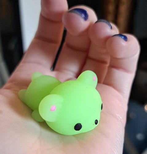Davey's tiny hand holds a neon green bear mochi, flopped and chilling on its tummy