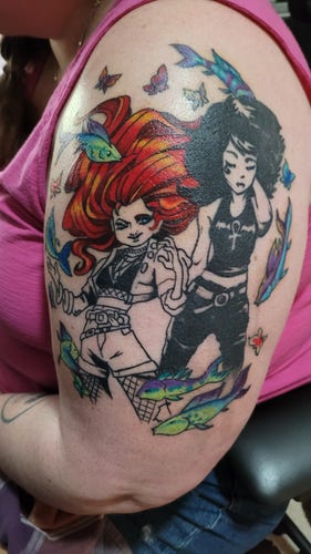 Large tattoo on a woman's upper arm. It is Death of the Endless (from the Sandman comic by Neil Gaiman) on the right in black and skin tones. Death looks serious and static. On the left is Delerium (from the same comic). Delerium is full of color with red hair that floats. She is kinetic and happy. Around them swirl full-color fish and butterflies.