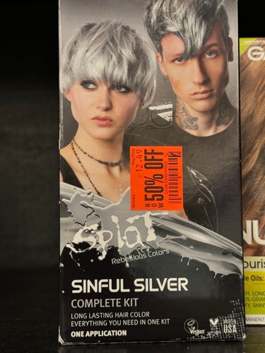 A box of hair coloring with two super cool people on the cover looking super serious in the silver hair and tattoos. The color is called "Sinful Surfer" and their hair is a very metallic silver. A big orange sticker has been applied stating "50% off", putting in doubt their coolness factor.