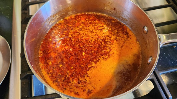 A stainless steel pot and frothing red sauce on a stove top.