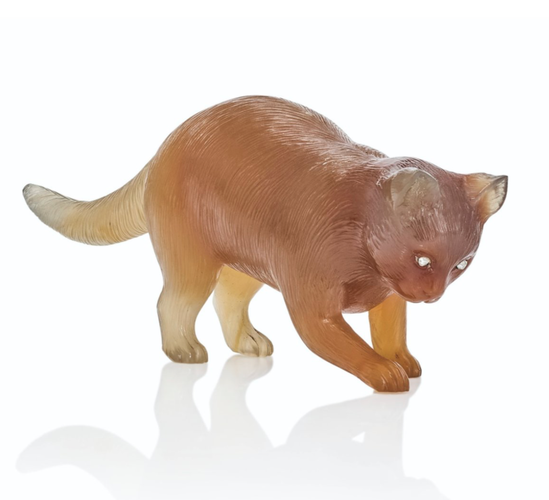 Color photo of a small translucent light brown model of a cat, standing with one paw extended as if in play. This is a close up of the cat showing the craftsmanship, impossibly tiny smooth grooves are cut into the surface to create fur texture. Each little toe is defined, the ears are sculpted flawlessly, the tiny diamond eyes glow white. According to the auction site it is only 2 1/2 inches long.