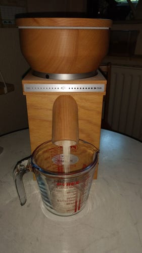 Kleine Kornmühle Fidibus (Komo) steht auf einem Tisch und mahlt Mehl. Davor steht ein Glasbehälter.