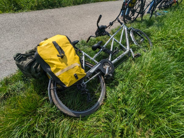 un vélo tandem gris avec des sacoches jaunes posé sur l'herbe au  bord d'un chemin de halage Amiénois.