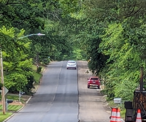 Photo of a residential street in a leafy neighborhood. 2/3 of the street width as been repaved; the remaining third is milled up and not being driven on.