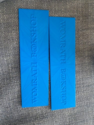 Two blue rectangular bookmarks with embossed text with very visible infill patterns