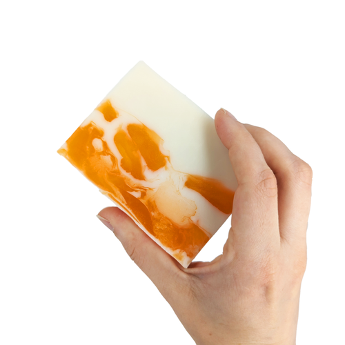 Hand holding a bar of white and orange soap