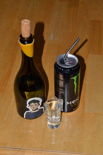Picture of a green bottle of Cdn. Wormwood Liquor with a shot glass in front of it, and an energy drink with a metal straw