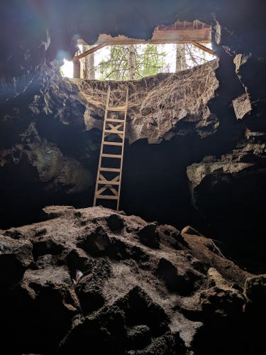 Standing below the mouth of a cave, with a wooden ladder reaching up into the normal world above.