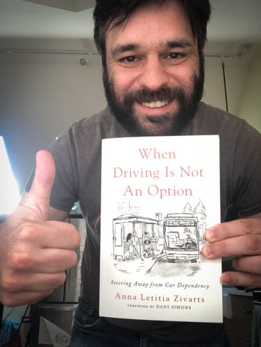 The author, a white man with a black beard, holding a copy of When Driving Is Not An Option while giving a thumbs up.