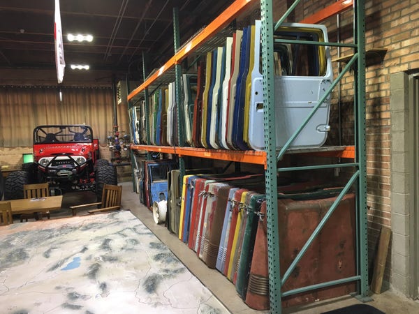 A corner of a warehouse has a large relief map on a table, a roofless Toyota in the corner, and large shelves holding doors and hoods.
