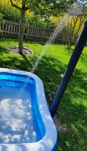Blue blowup swimming pool for kids getting filled with warm water from a solar garden shower.

