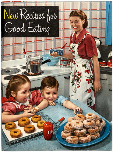 The cover of a vintage cookbook titled New Recipes for Good Eating. The cover has a photo of a woman frying donuts in her kitchen. Her two children reach for a pile of finished donuts. The woman has a smile that's far too wide and forced, like the Jack Nicholson version of The Joker.
