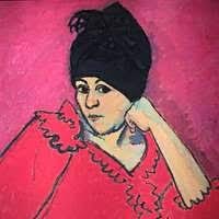 Dark Blue Turban 1910 - on a pinkish red background the subject wearing a black turban/headscarf looks quizzically at the viewer while resting her head on her arm