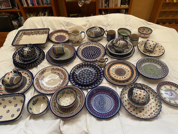 Assorted collection of painted ceramic dinnerware including plates, bowls, mugs, and serving dishes with various decorative patterns.
