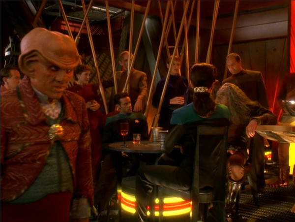 an image from the show, an old klingon regaling the crew and patrons of quark's bar, quark is on the left side with a sour expression on his face 