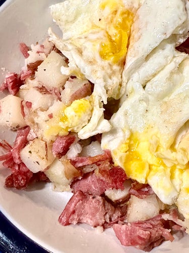 Closeup view of corned beef hash in bowl with two runny eggs on top. 