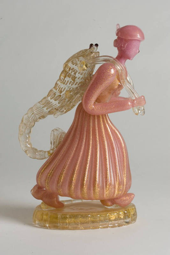 “This sculpture is of a woman with a featureless face, who carrying a large shrimp on her back. The woman is constructed of pink glass with gold inculsions while the shrimp and base are colorless glass with gold inclusions.”