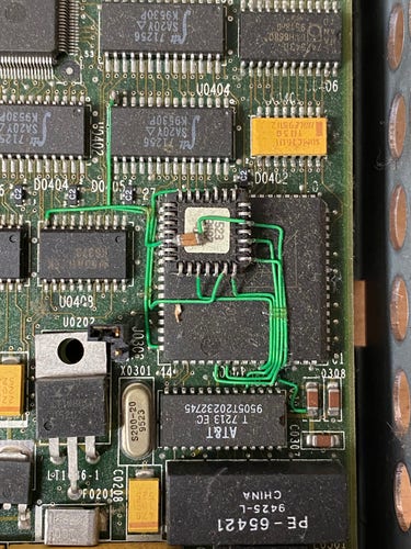 A factory bodge on a Sun SCSI/Ethernet combo card. A small PLCC package is upside down, glued to the top of another PLCC package, with a capacitor glued to its own top. Bodge wires run all all over the place from this ziggurat of silicon.