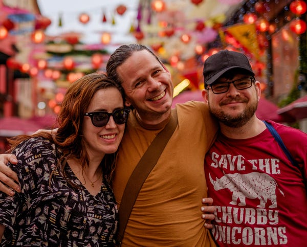 Portrait of three people standing in front of glowing red lights of a chinatown district.