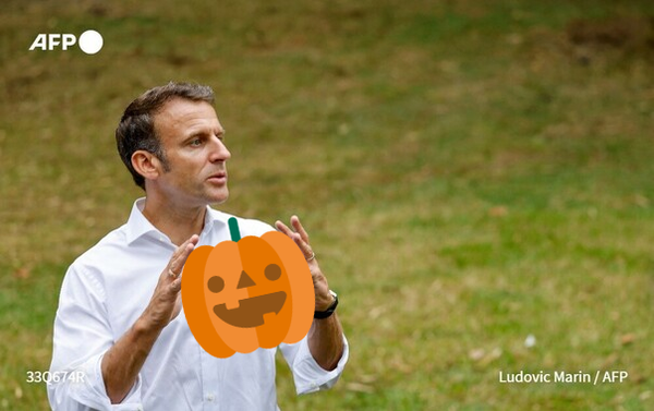 French leader Emmanuel Macron holding a large, cartoonish pumpkin with a Jack o'Lantern face carved into its front.